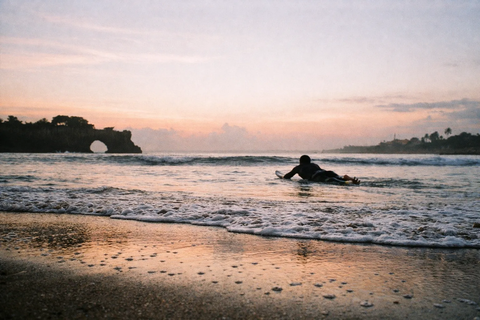 Silhouette of a surfer paddling out at Batu Bolong Beach at dawn