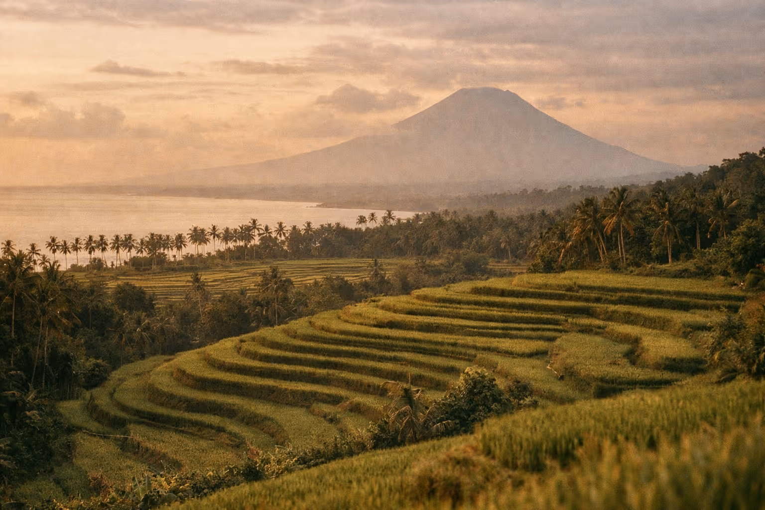 Editorial panorama of Bali at golden hour showing rice terraces, distant volcano, and coastline