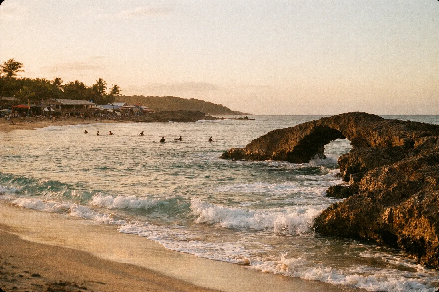 Sunset light over Jobos Beach showing lava-rock arches and distant surfers as silhouettes