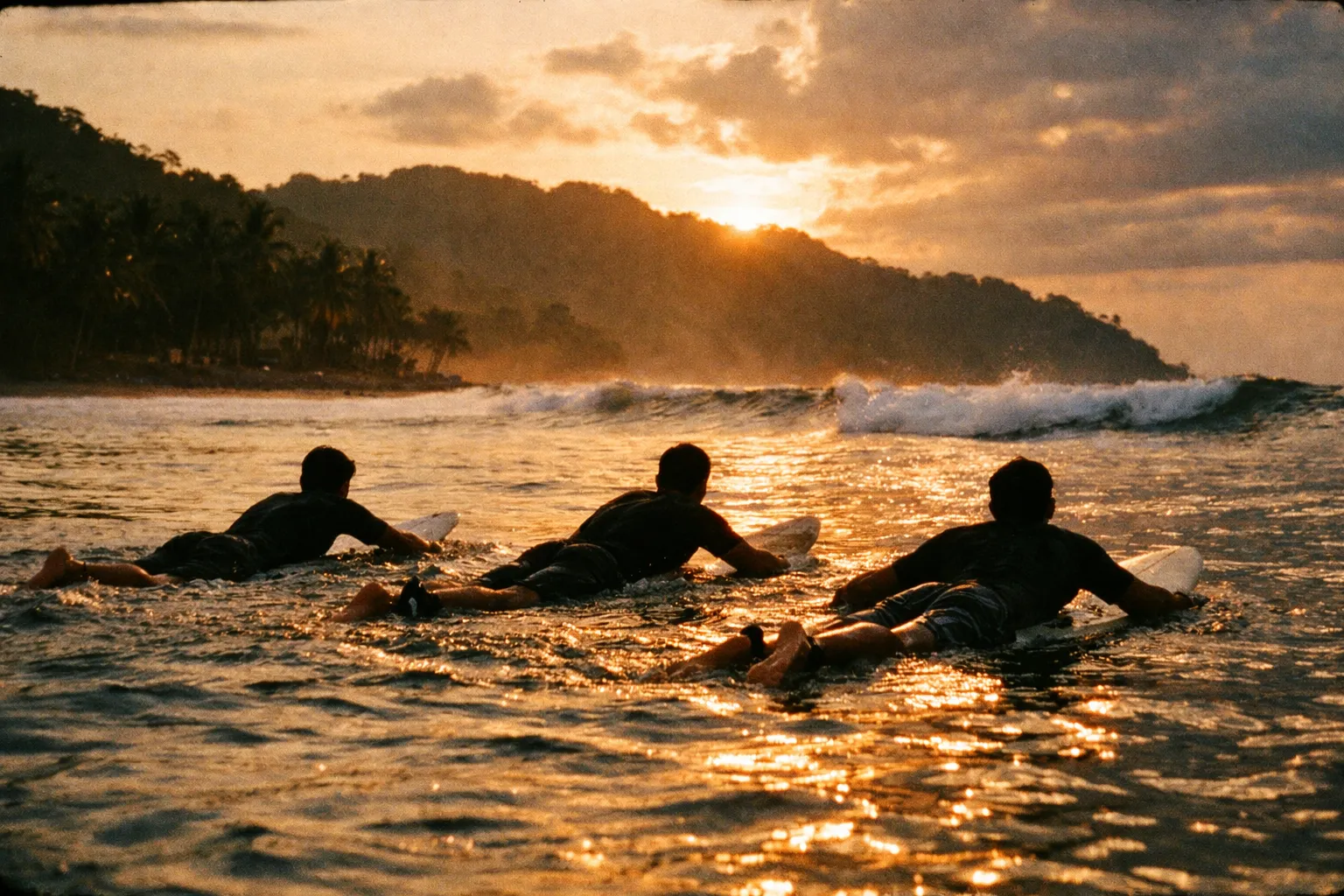Back-view silhouettes of surfers paddling and catching waves at a beach break, sunrise