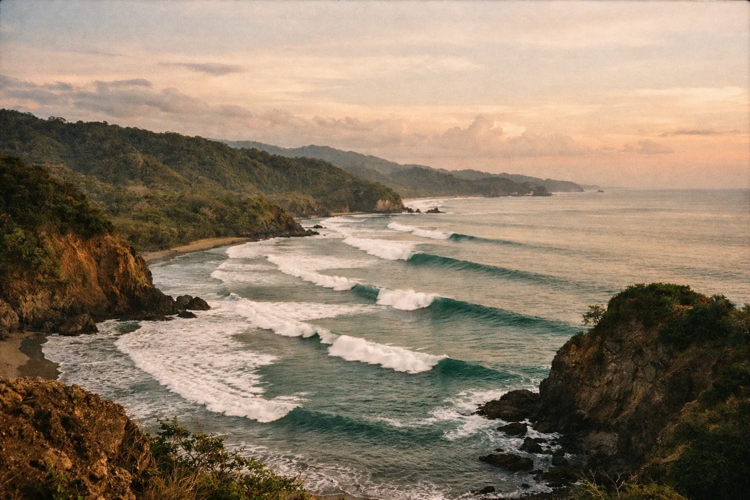 Wide coastal panorama showing multiple surf breaks along Costa Rica's Pacific coast with waves curling over rocky headlands at sunrise