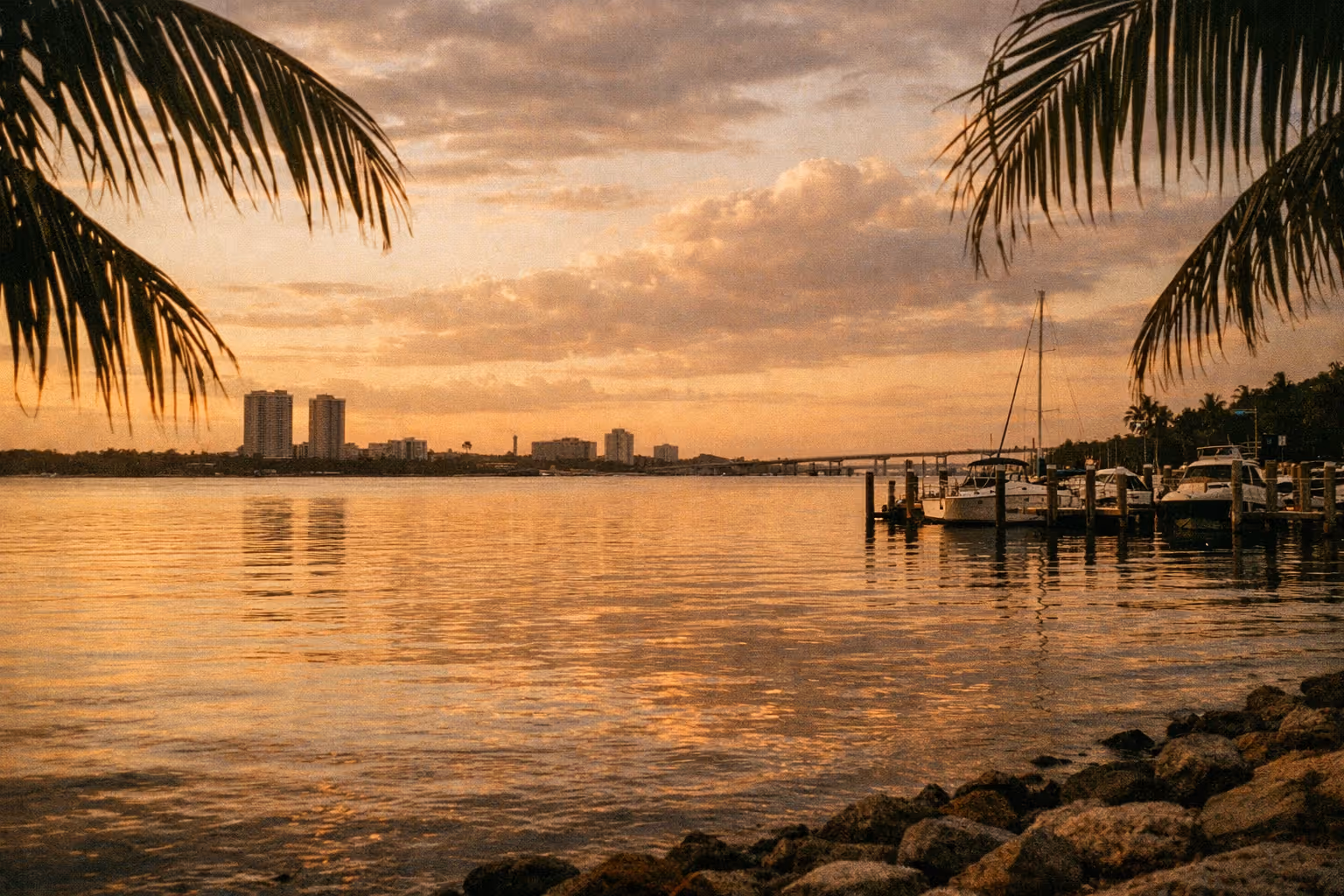Golden-hour Fort Myers waterfront with Caloosahatchee River, palm-lined bank, and distant riverfront skyline