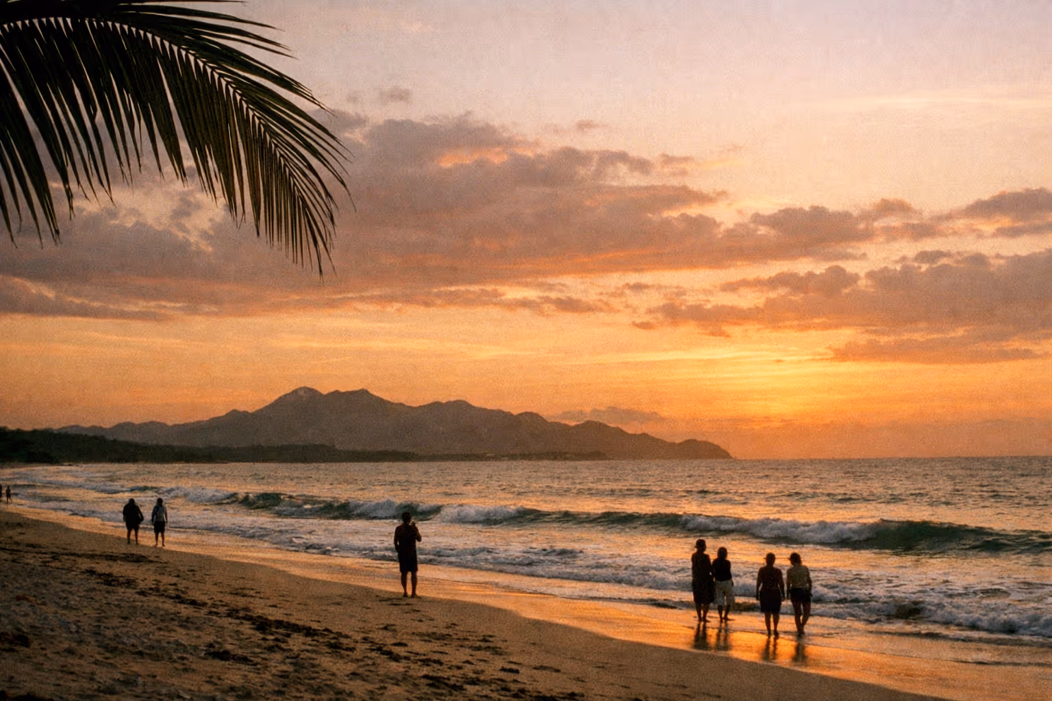 Golden-hour Guanacaste coastline with volcano silhouette and palm frond foreground