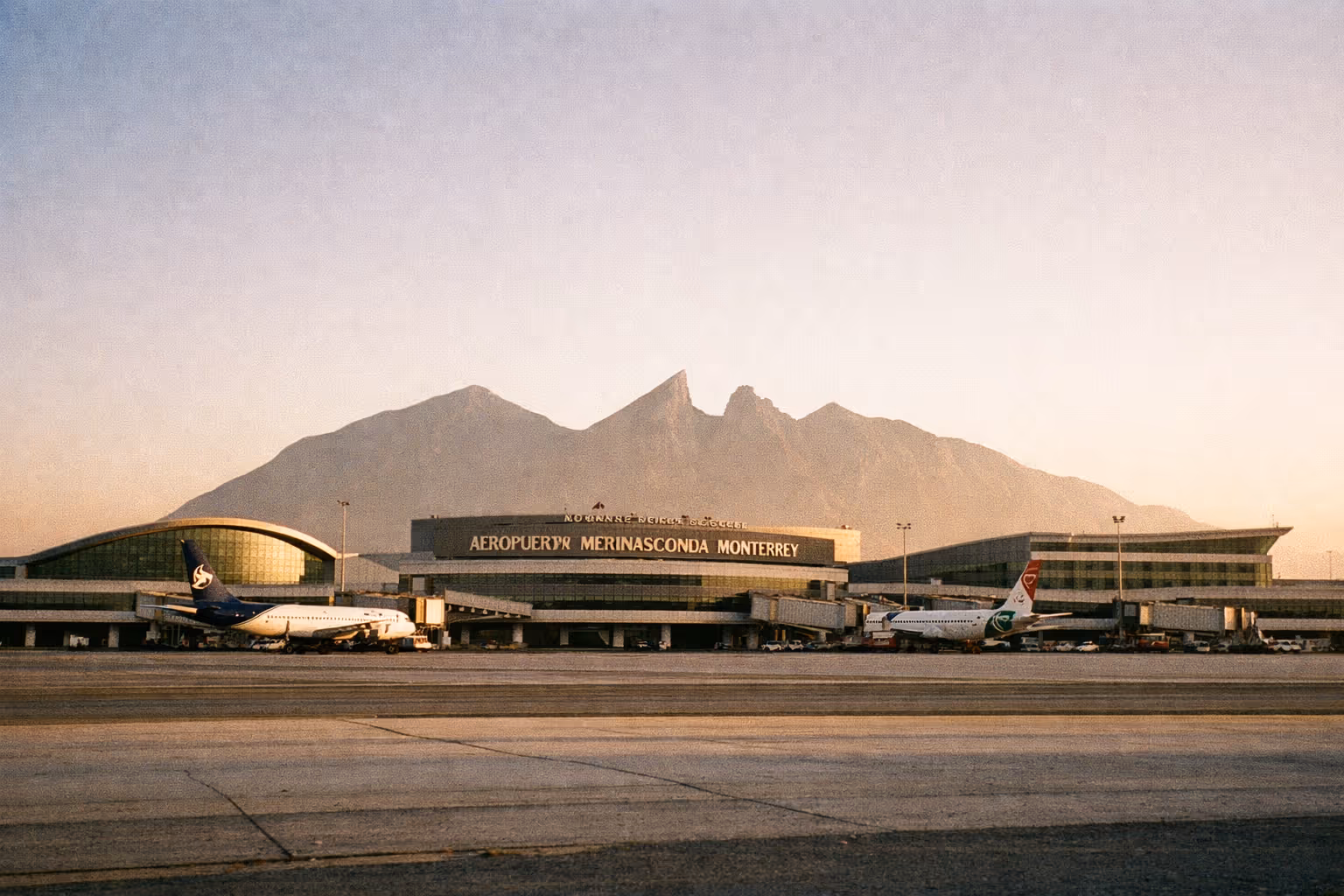 Editorial hero image: MTY airport at golden hour with three terminal wings and distant mountains
