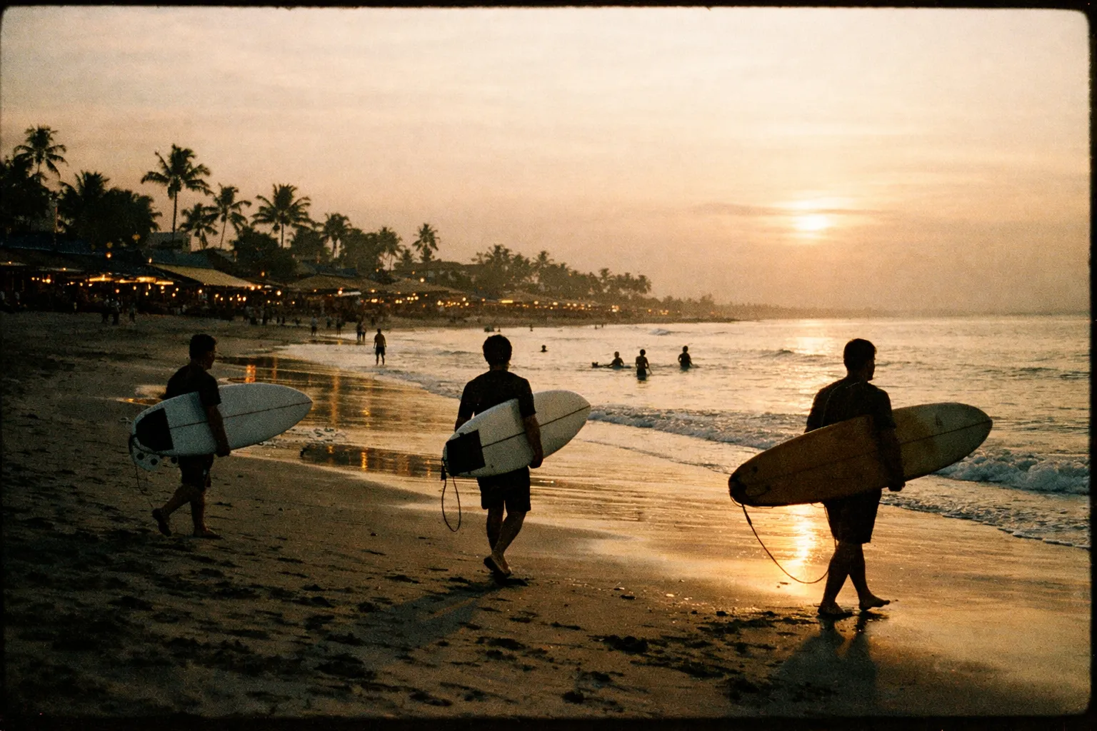 Silhouetted surfers walking along Seminyak Beach at golden hour